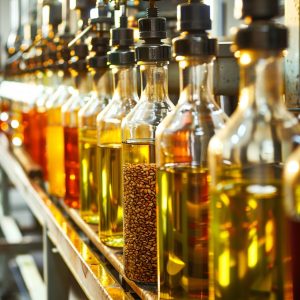 Row of glass bottles filled with a variety of cold pressed oils, illuminated under warm light.